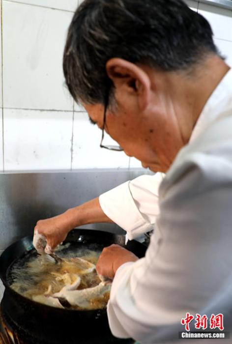 待油温七成热后，邓君秋两手分别拽着鲤鱼的尾巴和肚子下锅，让它在油锅中定型。