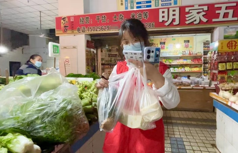 秦榕浚帮市民在菜市场选购蔬菜。蒋欢摄